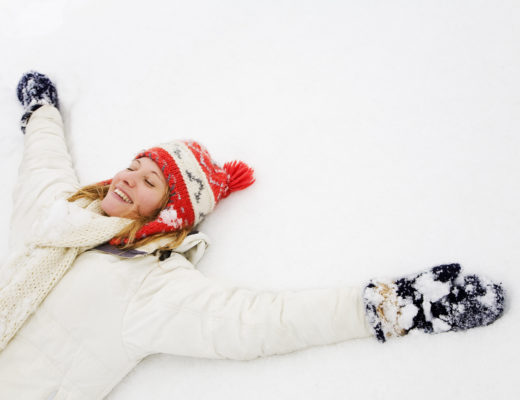 A happy girl is lying down in the snow and smiling.